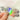 Holographic sticker reads "Feelings Club". Closeup of woman's hand with nude nailpolish holding sticker reflecting the light in a metallic rainbow color