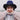 An Asian woman stands outside, holding her hands in front of her and making a heart shape with them. Her eyes are closed. She wears a dark blue felt hat and a stylish pink sweater. The 